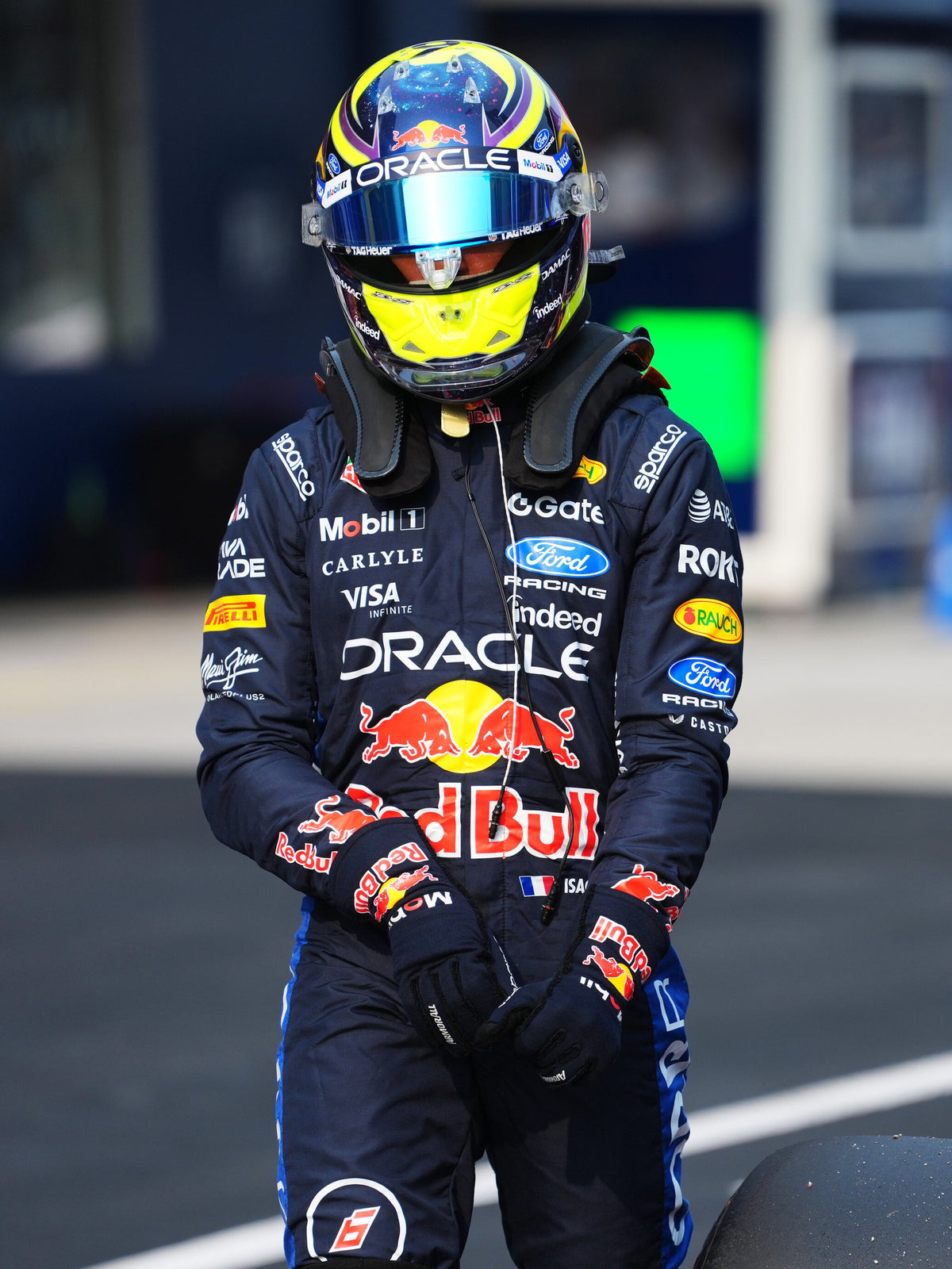 Isack Hadjar walking in his full-size 2026 helmet and Oracle Red Bull Racing race suit
