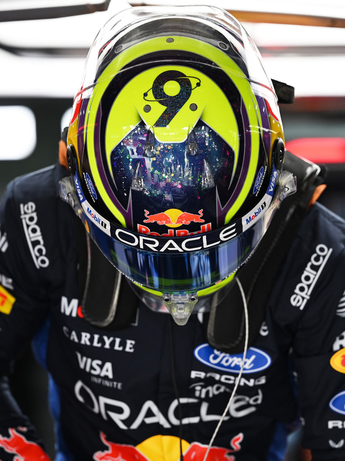 Isack Hadjar wearing his full-size 2026 helmet in the garage, the No. 6 in orbit on the crown